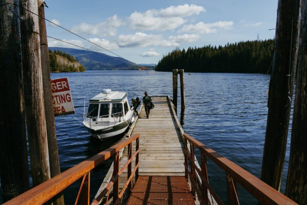 People walk down a wooden dock toward a small boat.