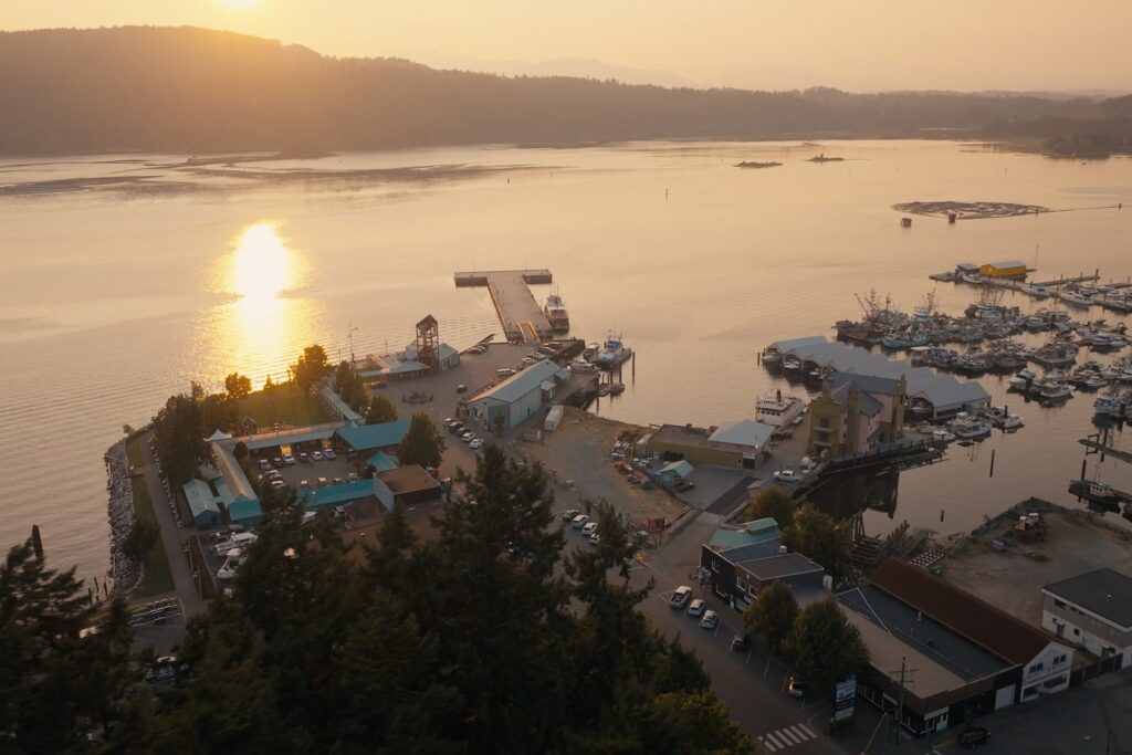 An aerial view of Port Alberni at sunset, with sunlight reflecting on the water near docks, boats, and waterfront buildings.