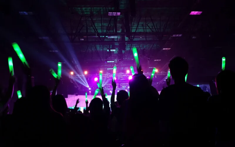 Crowd at concert : Silhouette people crowd happy and cheering with led foam stick light in front of bright colorful stage lights